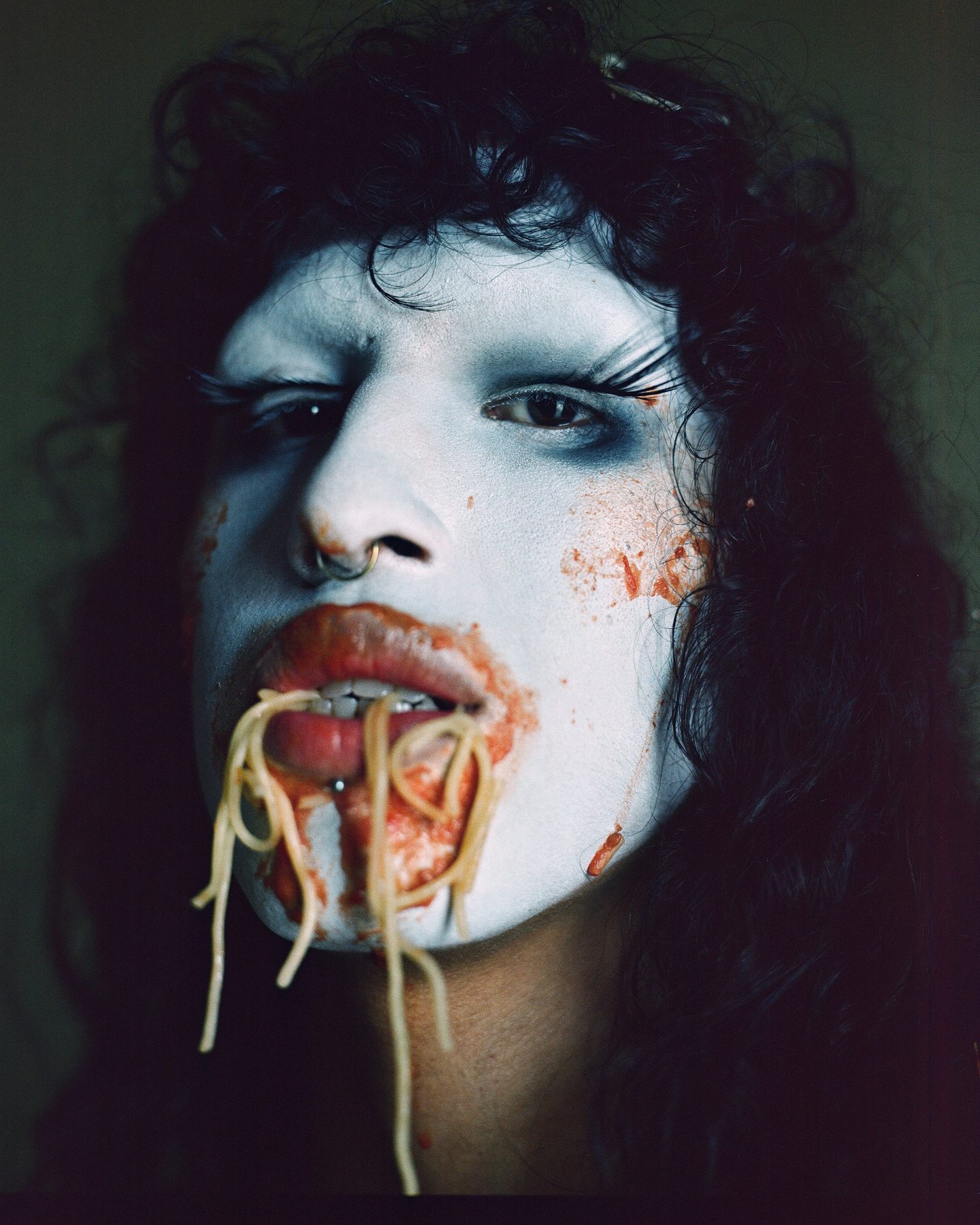 Close-up of wiqi in white face paint and a nose ring, with spaghetti and tomato sauce hanging from the mouth